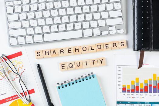 Shareholders equity concept with letters on cubes. Still life of office workplace with supplies. Flat lay white surface with computer keyboard and analytic report. Financial capital and investment.