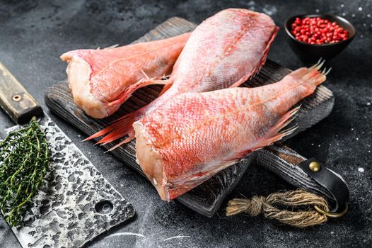 Raw Red perch or seabass fish on a cutting board. Black background. Top view.