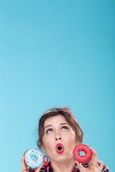 Junk food, diet and unhealthy lifestyle concept - pin-up woman with doughnuts over the blue background.