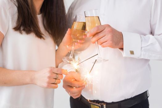 New year, holidays, date and valentines day concept - Loving couple holding sparklers light and glasses of champagne close-up over white background.