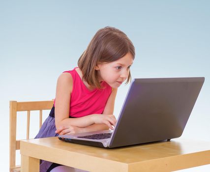 Little girl enthusiastically presses the keys laptop playing a computer game.