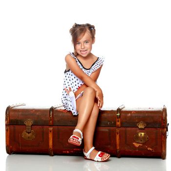 Little girl is sitting on a wooden box. Isolated on white background.