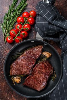 Grilled denver beef meat steak in a pan with rosemary. Dark background. Top view.