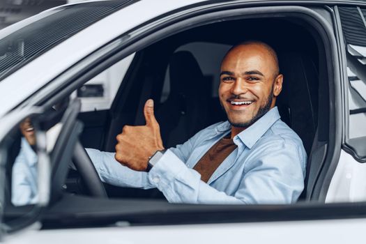 Portrait of a handsome happy African American man sitting in his newly bought car close up