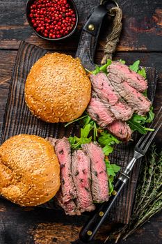 Burger with beef steak slices, arugula and spinach. Dark wooden background. Top view.