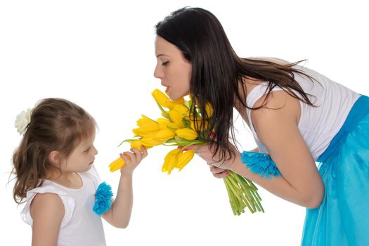 Beautiful young mother and little daughter in the same blue long skirts tutus , standing sideways to the camera ,admiring the bouquet of yellow tulips.Little girl enjoying the smell of flowers.Isolated on white background.