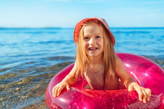 Happy little girl bathing in sea with pink circle and hat