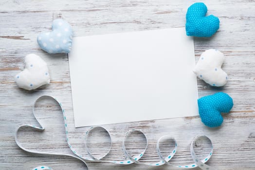 Flat lay composition with blue and white love hearts. Blank sheet of white paper on vintage wooden table. Declaration of love letter. Saint Valentine's day congratulation. Romantic event invitation.