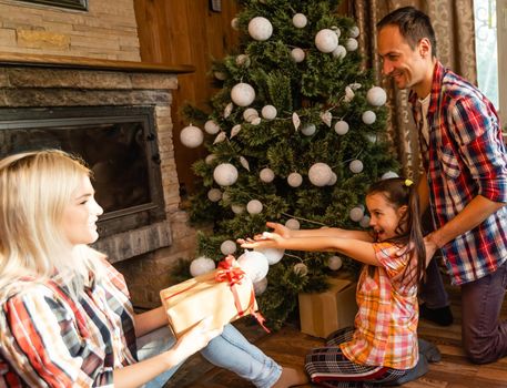 Theme Christmas and New Year family circle. Young Caucasian family sitting on wooden floor home in living room near fireplace Christmas tree.