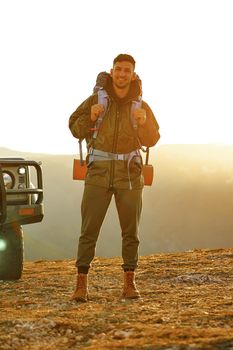 Portrait of a young traveler man in hiking equipment standing near his off-road car at dawn