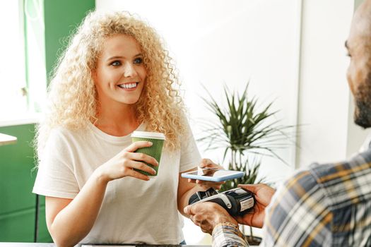 Woman customer of coffee shop paying for coffee through mobile phone using contactless technology close up