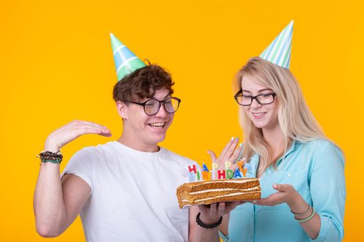 Young cheerful students charming girl and nice guy in greeting paper caps holding a cake with a bengal sparks candle. Concept of congratulations on the holiday and anniversary