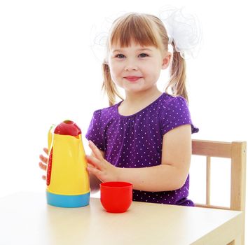 Happy childhood, adolescence, the development of the family concept.Little girl sitting at the table pouring from a plastic tea kettle. Isolated on white background.