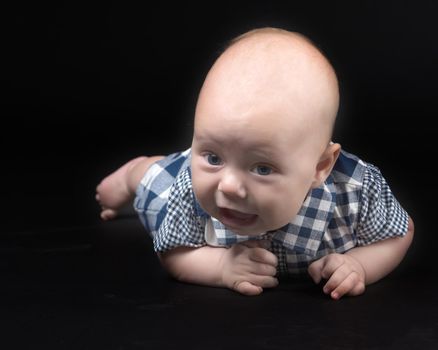 A charming baby lies on the blanket and looks into the camera on a black background. The concept of a happy childhood, the birth and upbringing of a child.