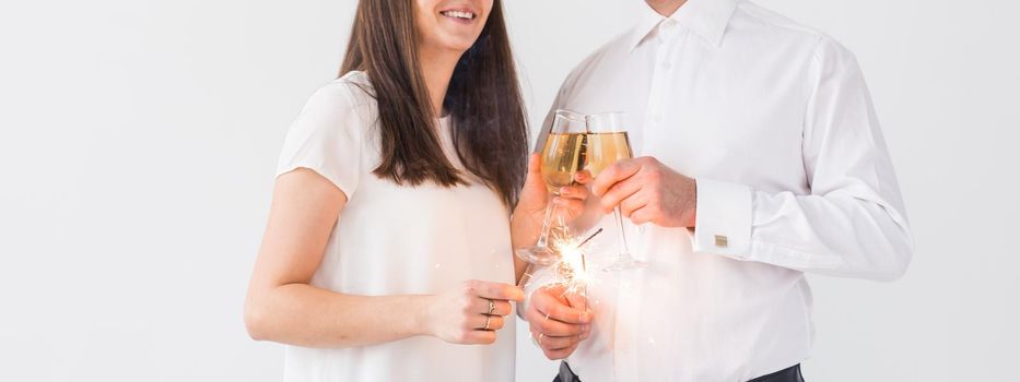 New year, holidays, date and valentines day concept - Loving couple holding sparklers light and glasses of champagne close-up over white background.