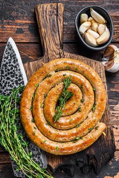 BBQ spiral sausage from pork and beef meat on a wooden cutting board. Dark wooden background. Top view.