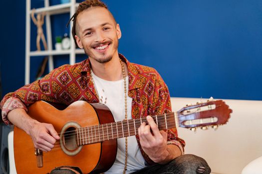 Young stylish guy musician playing guitar in his apartment close up