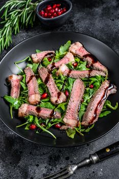 Grilled Beef Steak salad with arugula, pomegranate and greens vegetables. Black background. Top view.