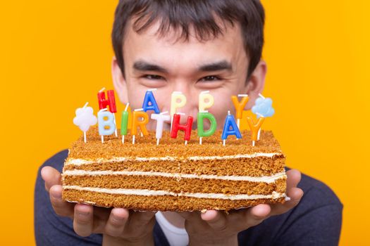 Funny positive guy in glasses holds in his hands a cake with the inscription happy birthday posing on a yellow background. Concept of holidays and anniversaries. Advertising space