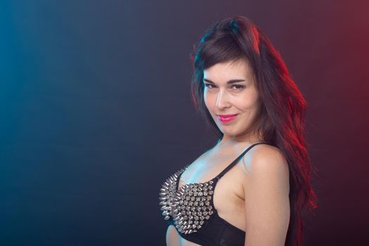 Beautiful young sexy brunette woman posing on a dark background in a riveted top on a dark background. The concept of grooming and attractiveness