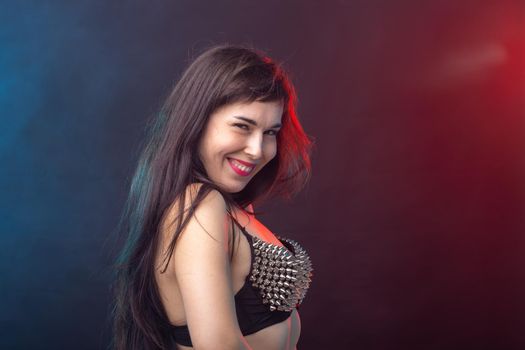 Beautiful young sexy brunette woman posing on a dark background in a riveted top on a dark background. The concept of grooming and attractiveness