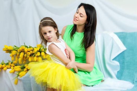 Beautiful young mother and little daughter on the sofa with a bouquet of flowers.