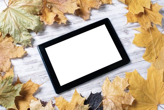 Tablet computer with blank screen lies on vintage wooden desk with bright foliage. Flat lay composition with autumn leaves on white wooden surface. Internet communication and digital technology