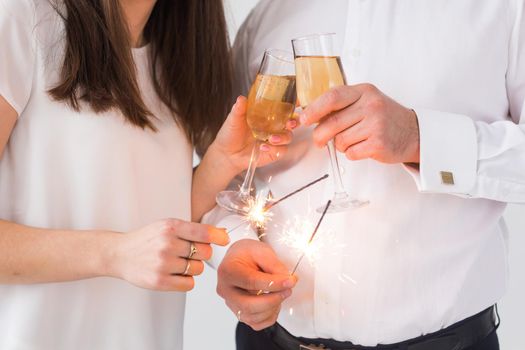 New year, holidays, date and valentines day concept - Loving couple holding sparklers light and glasses of champagne close-up over white background.