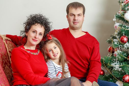 Happy parents with little daughter in a relaxed family atmosphere in the New year.Around the Christmas tree.