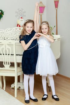 2 beautiful little girls are twins, show a heart around a big white Grand piano .