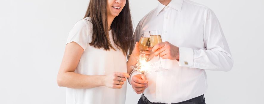 New year, holidays, date and valentines day concept - Loving couple holding sparklers light and glasses of champagne close-up over white background.