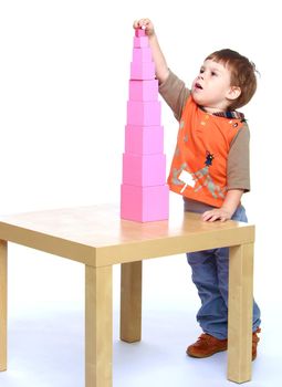 Boy builds pink tower in Montessori school.Isolated on white background portrait.