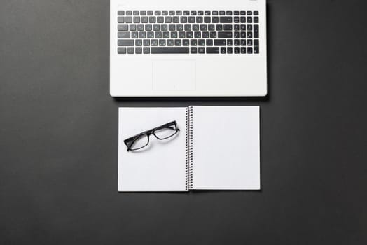 Still life of office workplace with supplies and copy space. Flat lay black surface with laptop computer and open blank notebook. Paperwork, audit and accounting. Top view modern office workspace.