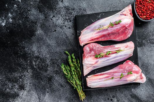 Raw lamb shanks meat on a marble board. Black background. Top view. Copy space.