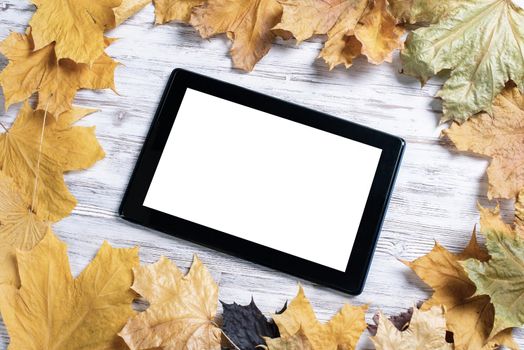 Tablet computer with blank screen lies on vintage wooden desk with bright foliage. Flat lay composition with autumn leaves on white wooden surface. Internet communication and digital technology