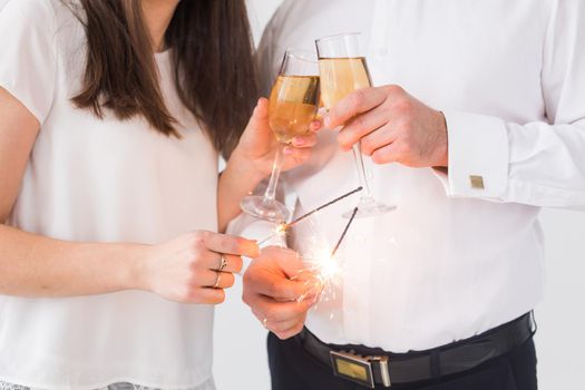 New year, holidays, date and valentines day concept - Loving couple holding sparklers light and glasses of champagne close-up over white background.
