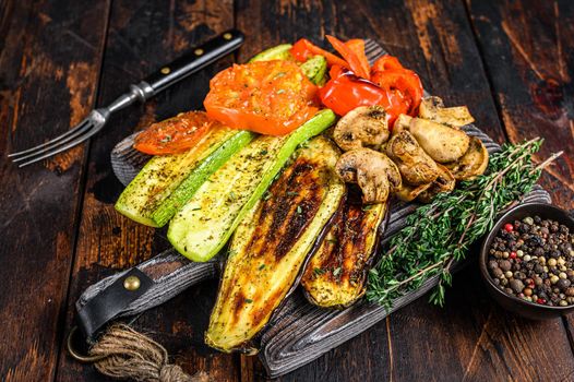 Grilled vegetables bell pepper, zucchini, eggplant and tomato with dry herbs on a wooden board. Dark wooden background. Top view.