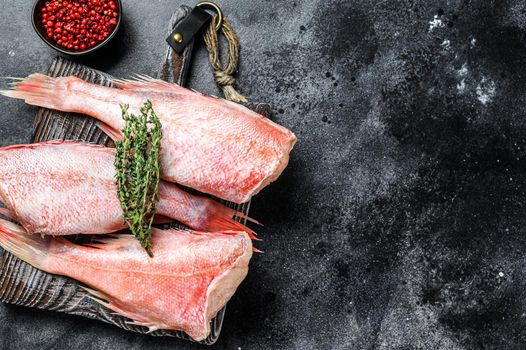 Whole raw red snapper fish on a cutting board. Black background. Top view. Copy space.