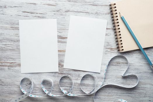 White paper and sketchbook with pen on wooden table. Flat lay elegant composition with ribbon in shape of heart. Happy birthday or anniversary card. Romantic Saint Valentine's day congratulation