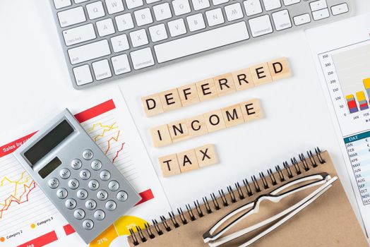 Deferred income tax concept with letters on cubes. Still life of office workplace with supplies. Flat lay white surface with computer keyboard and financial report. Capital management andaccounting.