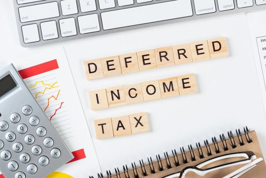 Deferred income tax concept with letters on cubes. Still life of office workplace with supplies. Flat lay white surface with computer keyboard and financial report. Capital management andaccounting.