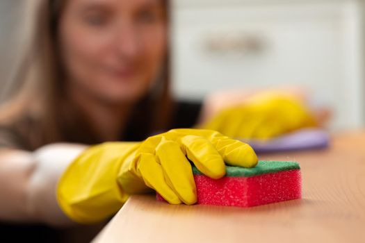 Unrecognizable woman in yellow gloves wiping wooden table top close up