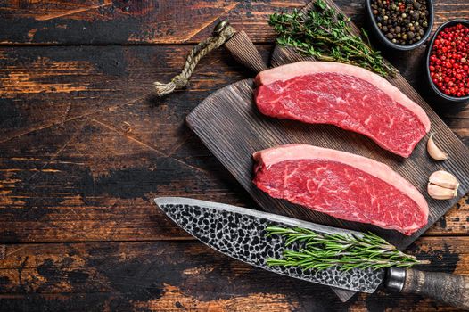 Raw top sirloin beef meat steak on a cutting wooden board. Dark wooden background. Top view. Copy space.