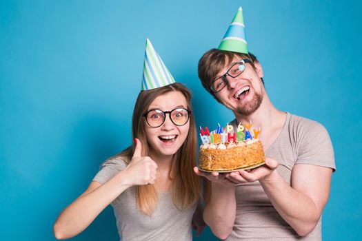 Young cheerful students charming girl and nice guy in greeting paper caps holding a cake with a bengal sparks candle. Concept of congratulations on the holiday and anniversary