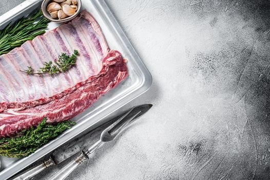 Uncooked raw rack of lamb ribs in baking dish with herbs. White background. Top view. Copy space.