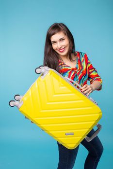 Joyful smiling young brunette woman posing with a yellow suitcase while waiting for a vacation. The concept of tourism and travel to warm countries. Copyspace