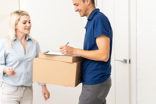 woman receiving boxes from postman at the door in home delivery concept. Woman received the parcel from the postman at home. Postman giving cardboard box to young woman.