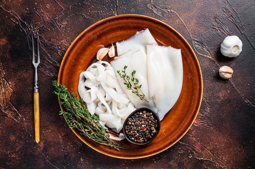 Sliced raw rings squid in a rustic plate with rosemary. Dark background. Top view.