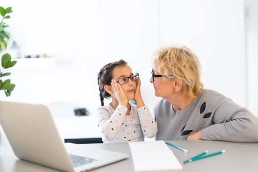 Cute and happy little girl child using laptop computer with her grandma, studying through online e-learning system.