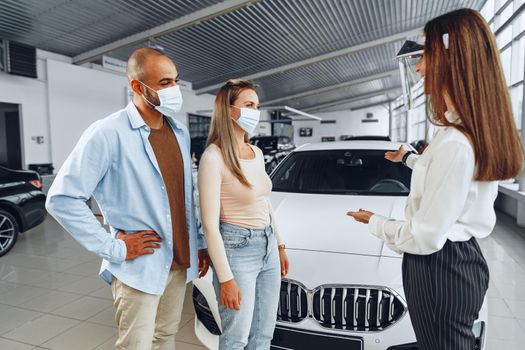 Woman car dealer consulting buyers wearing medical face shield. Coronavirus job requirements concept